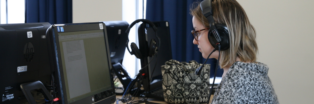 Une étudiante assise devant l'ordinateur avec des écouteurs dans le laboratoire des langues.